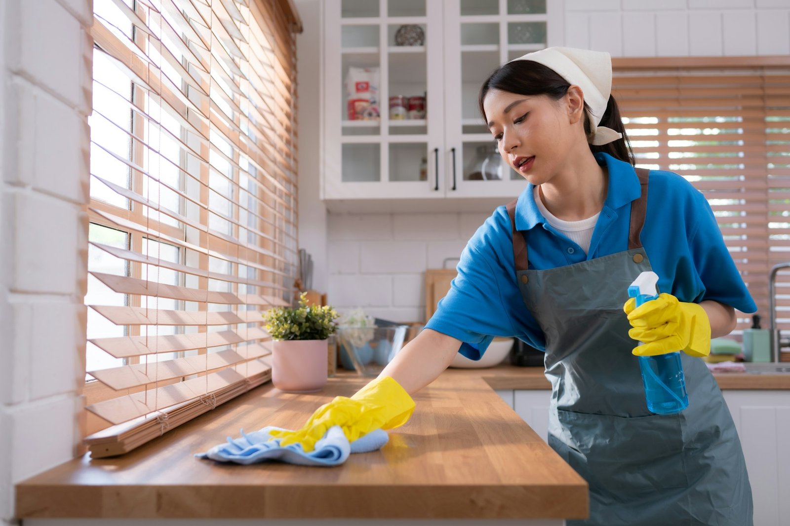 Cleaning service. Close-up of woman in apron and rubber gloves cleaning wooden table with spray